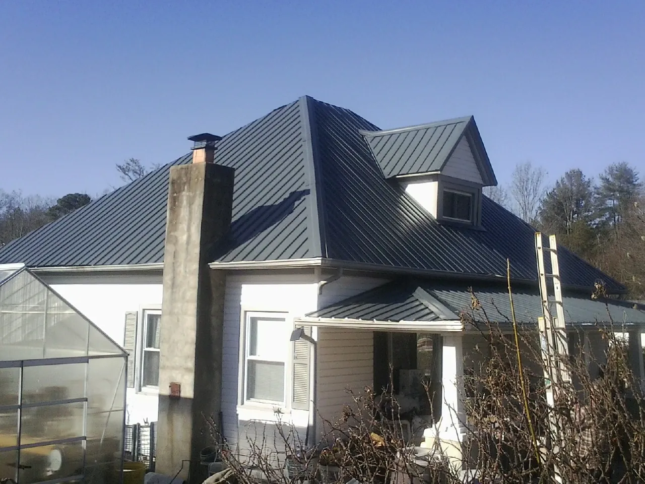Dark blue standing seam metal roof on a white farmhouse with dormer — Slate & Tile Roof Repair by Roofing Brothers in Mandan
