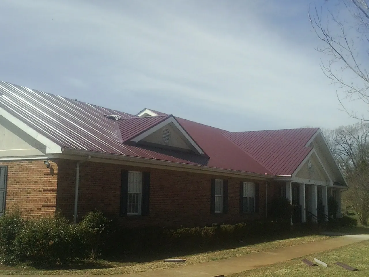 Red metal roof with gabled entries on a long brick building, from a Hail Damage Roof Repair job in Mandan