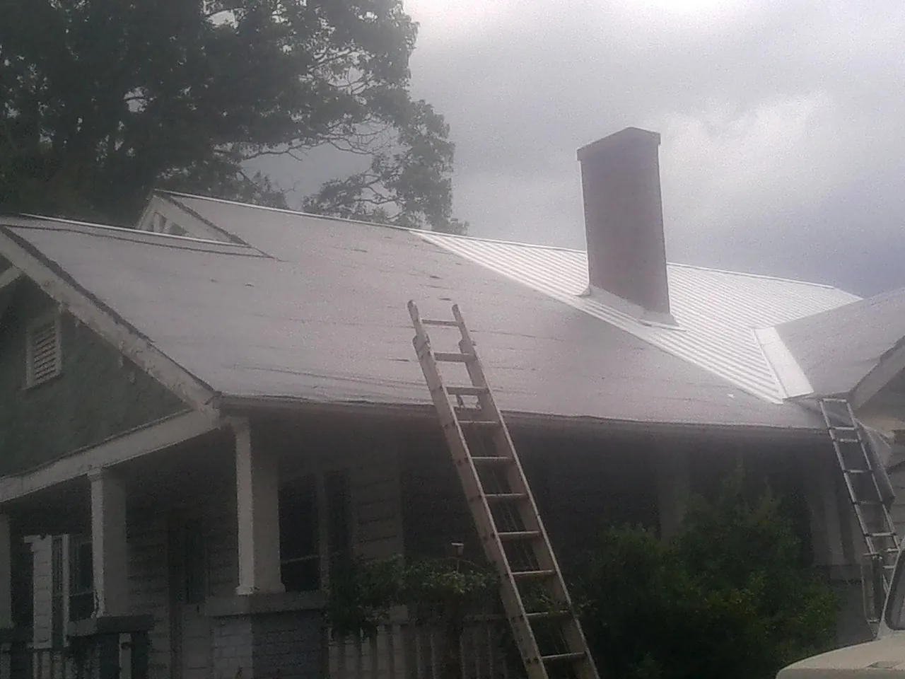 Ladders against a metal roof on an older home with a brick chimney in Mandan