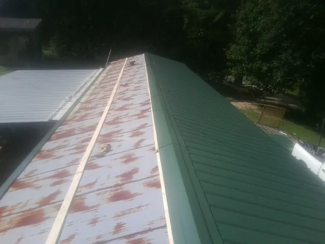 Old rusted panels beside newly installed green metal roofing — Wind Damage Roof Repair by Roofing Brothers in Mandan
