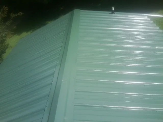 New green metal panels meeting at the ridge of a roof — Flat Roof Repair work by our crew in Mandan