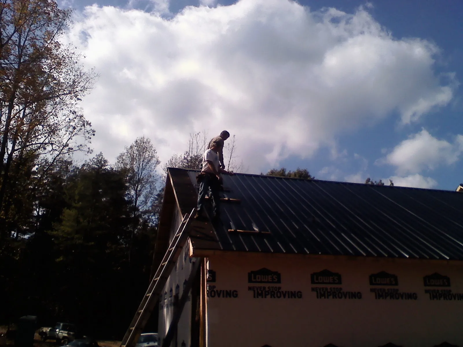 Roofer fastening dark metal panels high against a cloudy sky, from a Roof Inspection job in Mandan